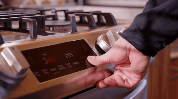 A man's hand, with thumb visible, starts a silver oven with a black touch screen, setting it to 365 degrees.