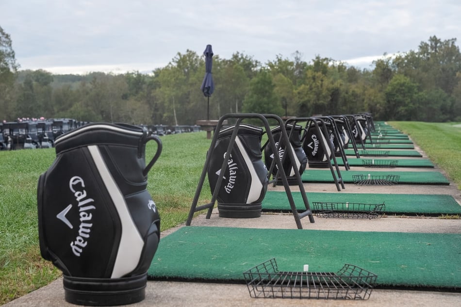 Rows of golf practice stations with Callaway golf bags along a green driving range for the Lift As We Climb Golf Tournament.