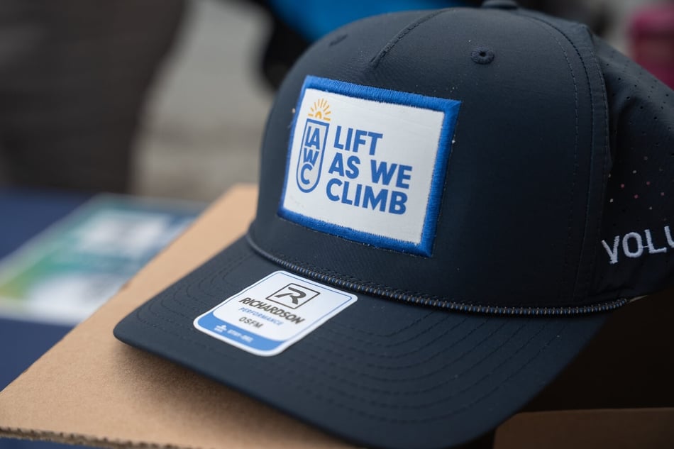 Black hat featuring a blue and white "Lift As We Climb" logo patch.