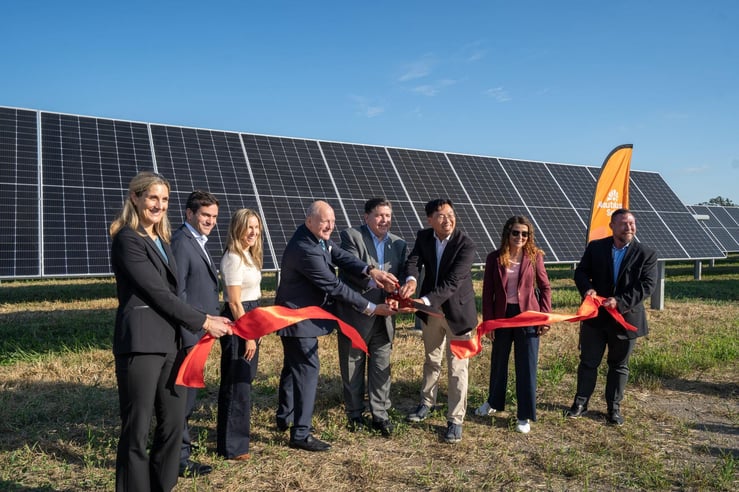 Group of officials, including Governor JB Pritzker, Nautilus Solar CEO Jeffrey Cheng, and Power Sustainable CEO Bruce Heyman, cutting a ceremonial red ribbon in front of solar panels at a solar farm.