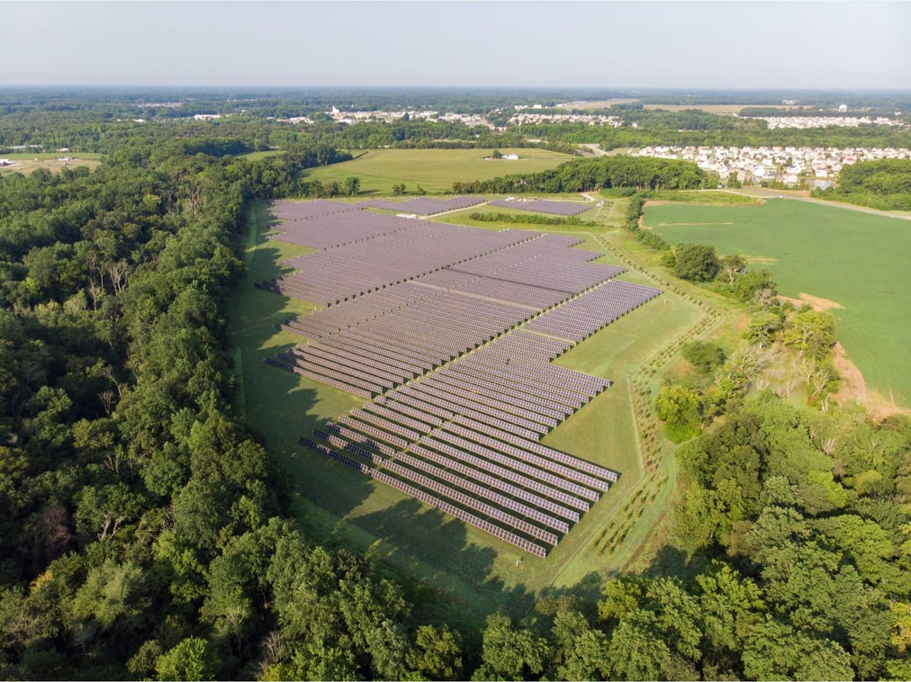 Aerial shot of a large community solar farm in Dover, Delaware surrounded by lush green trees and fields.