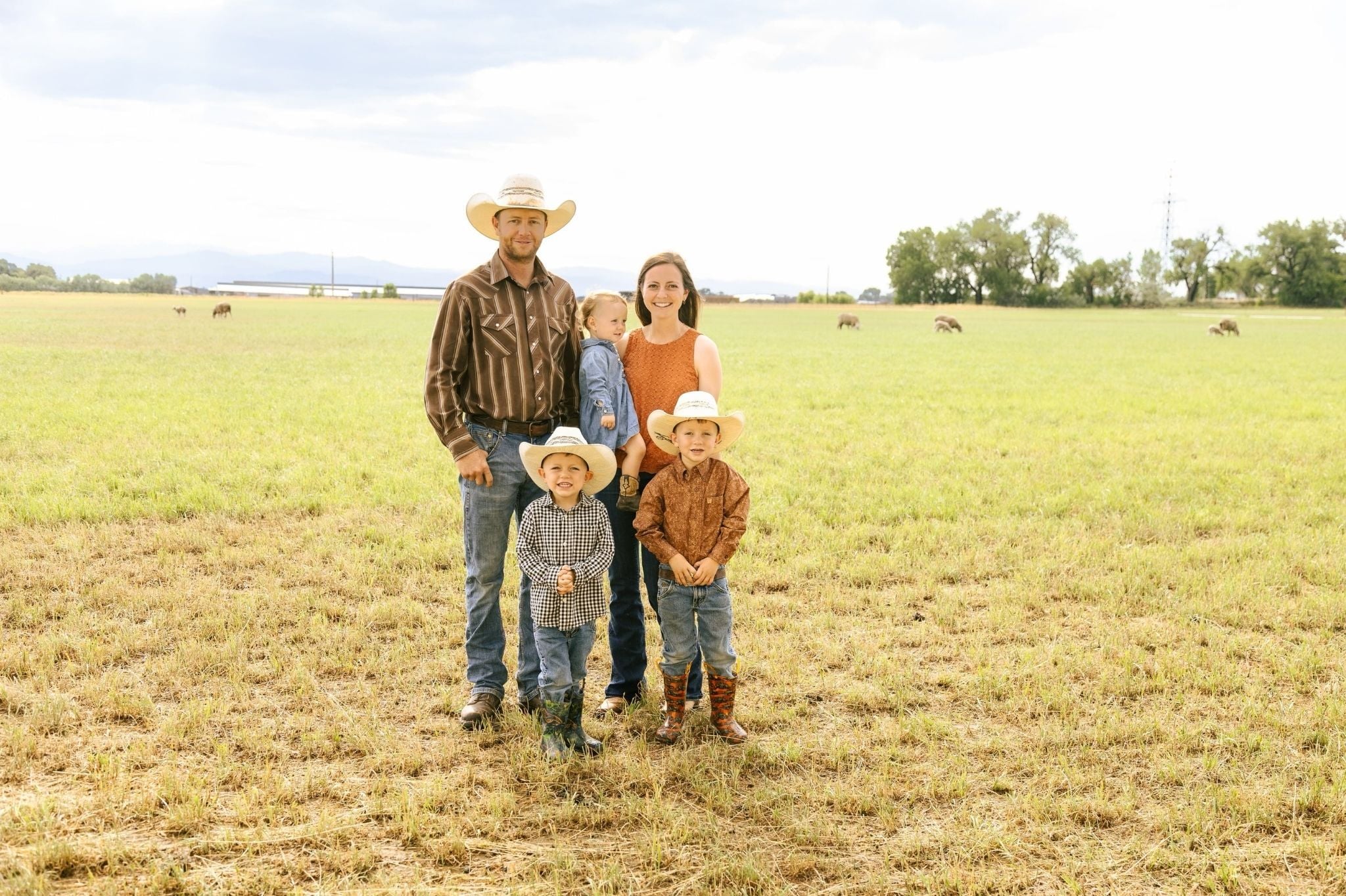 Tom Brown and his family wearing cowboy hats standing together in an open grassy field with grazing animals in the distance.