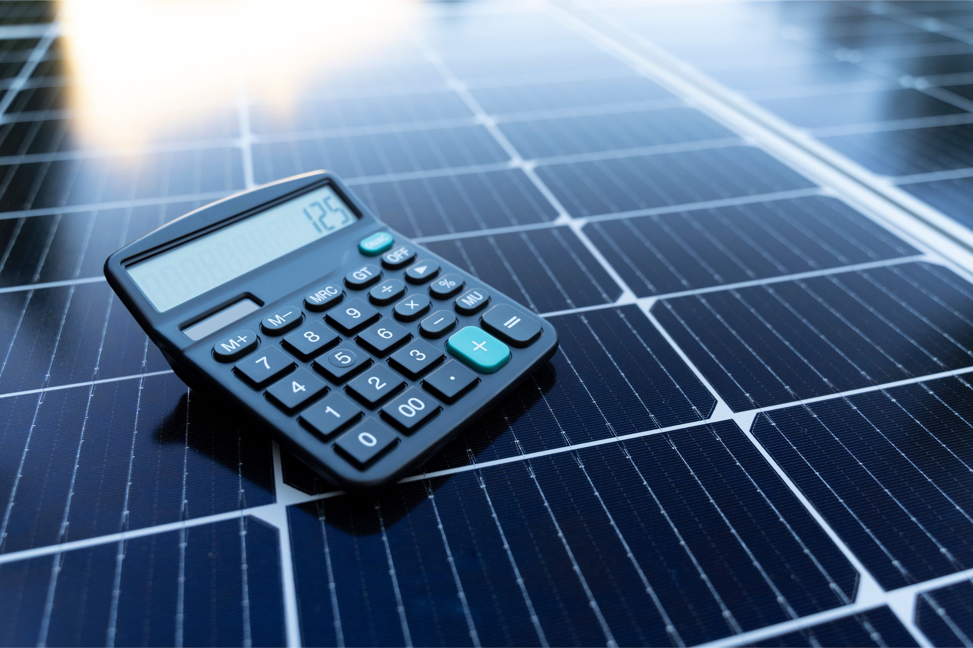 Black calculator resting on a solar panel, symbolizing cost calculations and savings related to solar energy.