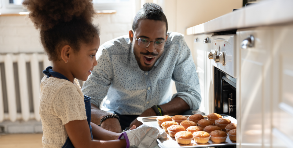 father smiling at daughter putting muffins in an oven